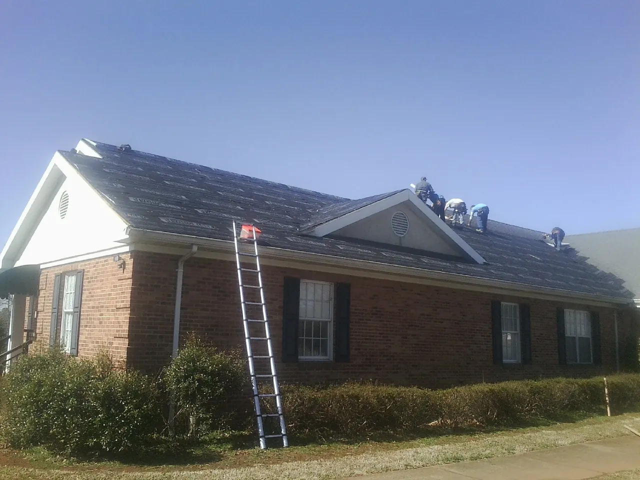 Crew tearing shingles off a brick ranch roof with a ladder set — Emergency Roof Repair work by our crew in Marseilles