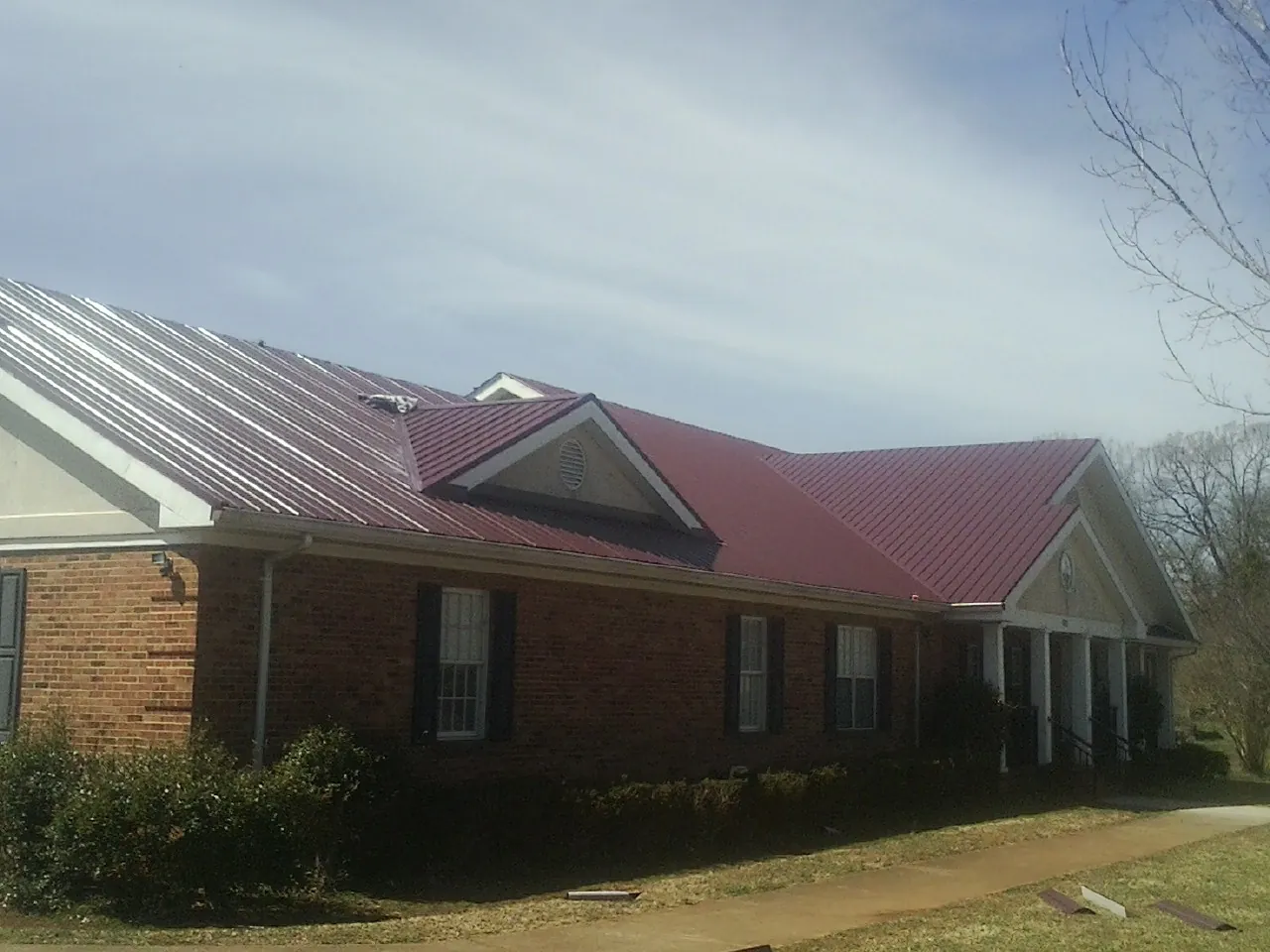 Red metal roof with gabled entries on a long brick building, from a Hail Damage Roof Repair job in Marseilles