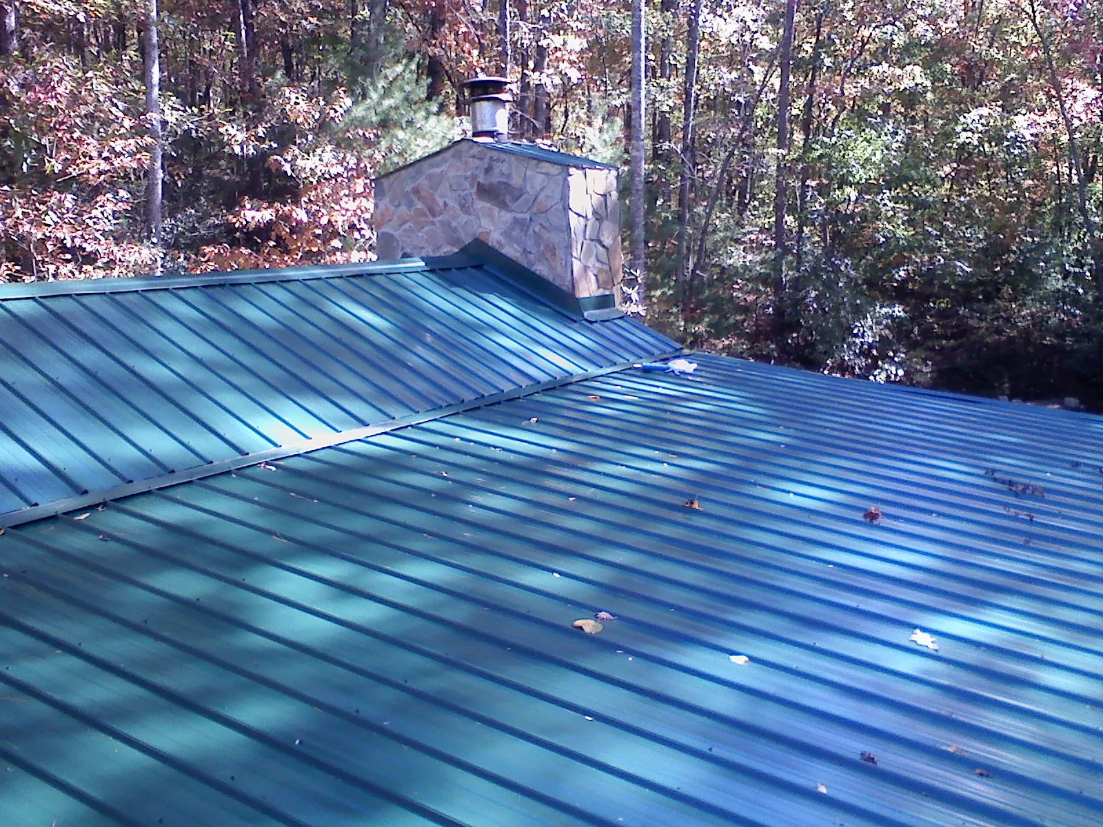 New green metal roof and stone chimney surrounded by autumn woods in Marseilles