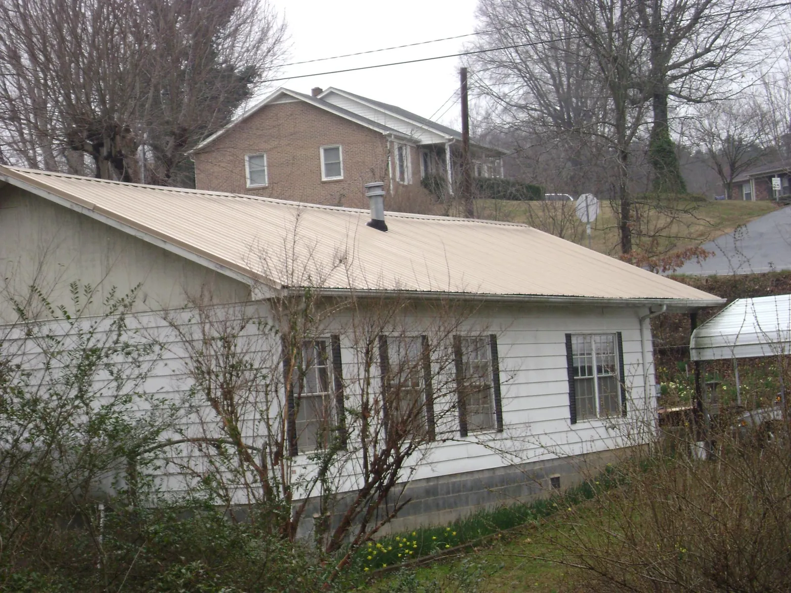 Tan metal roof on a white sided house set into a hillside — Commercial Roofing by Roofing Brothers in Marseilles