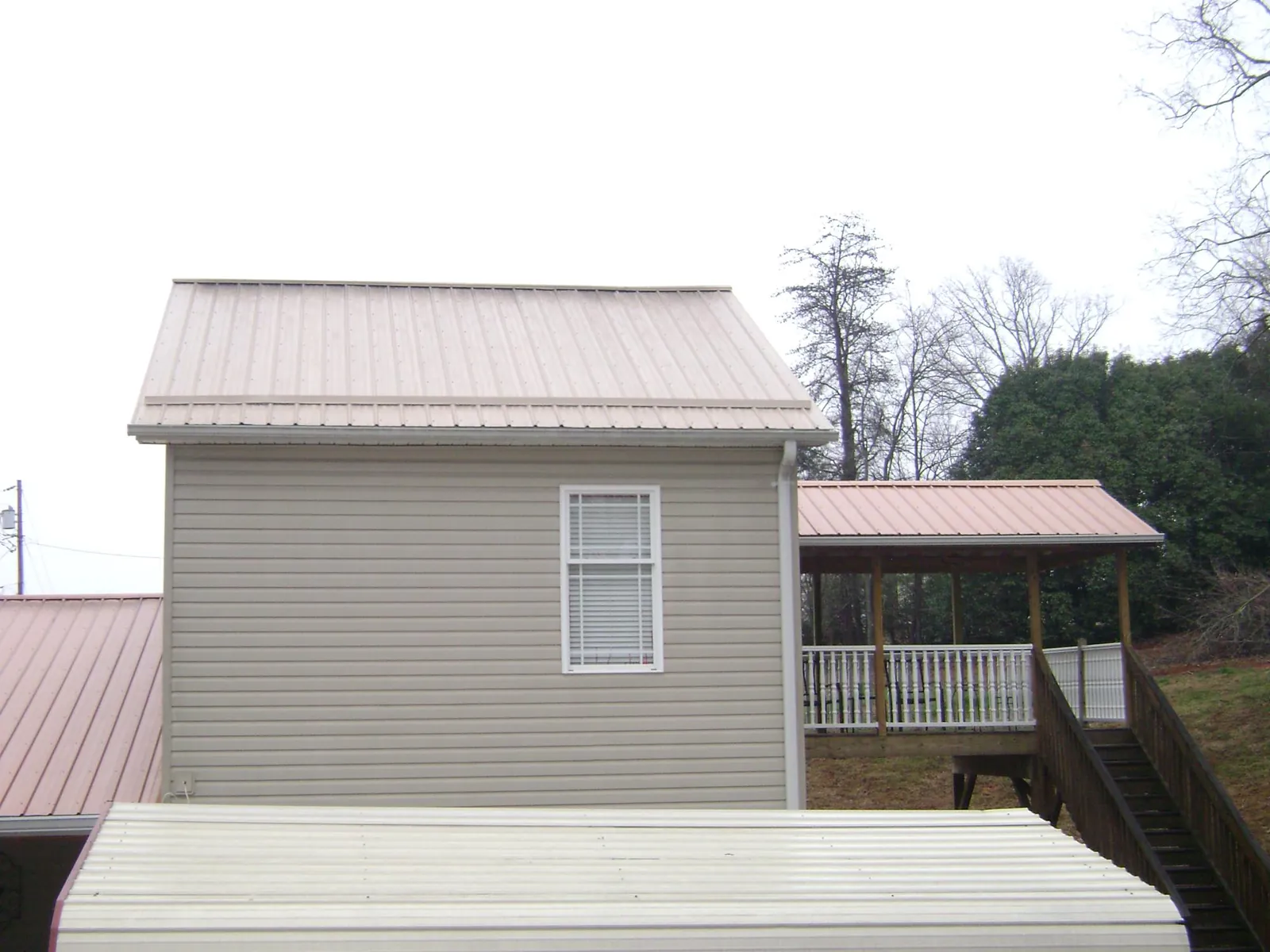 Tan metal roofs on a two story addition and attached porch, from a Roof Replacement job in Marseilles